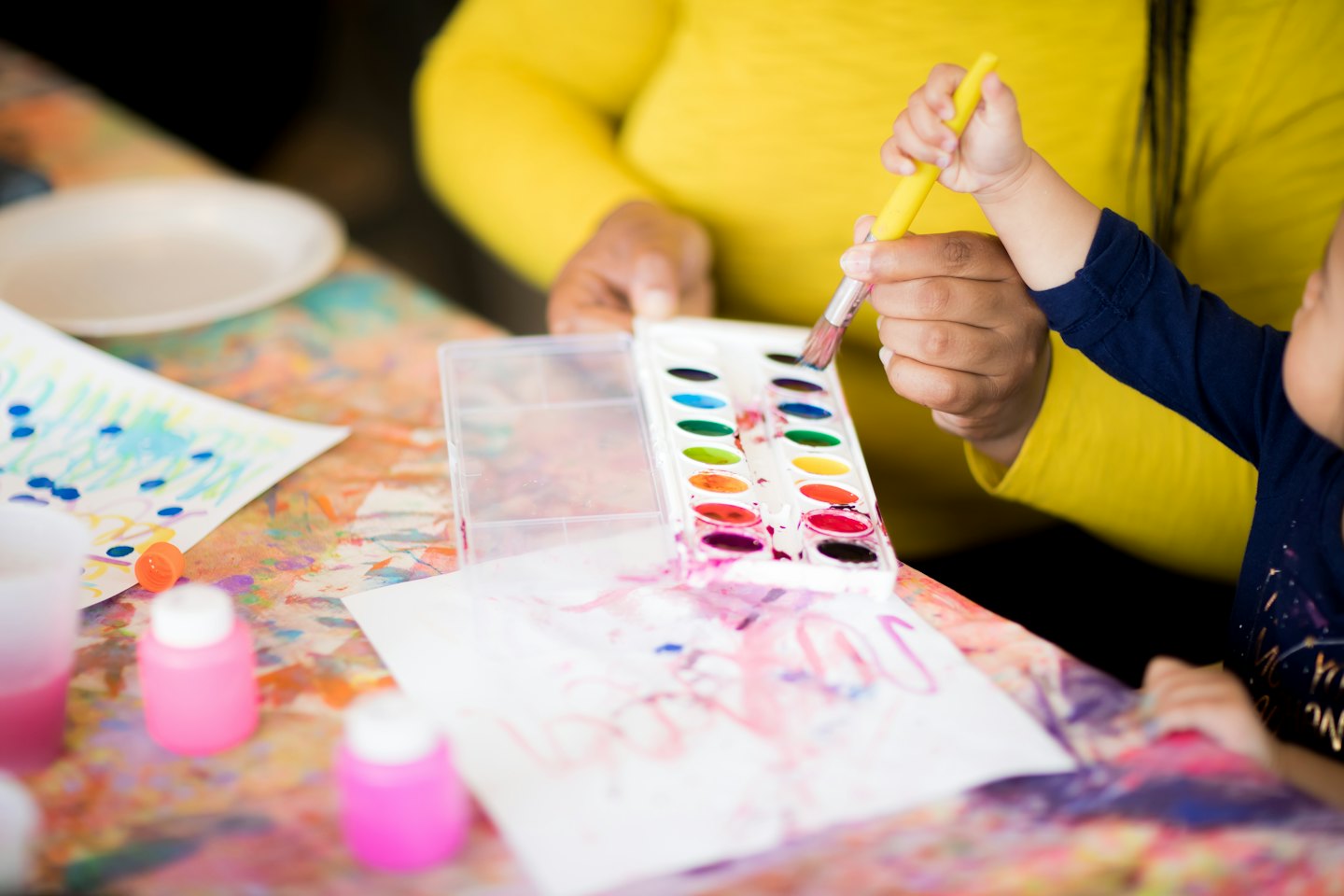 Un adulto guida la mano di un bambino mentre dipinge su carta.
