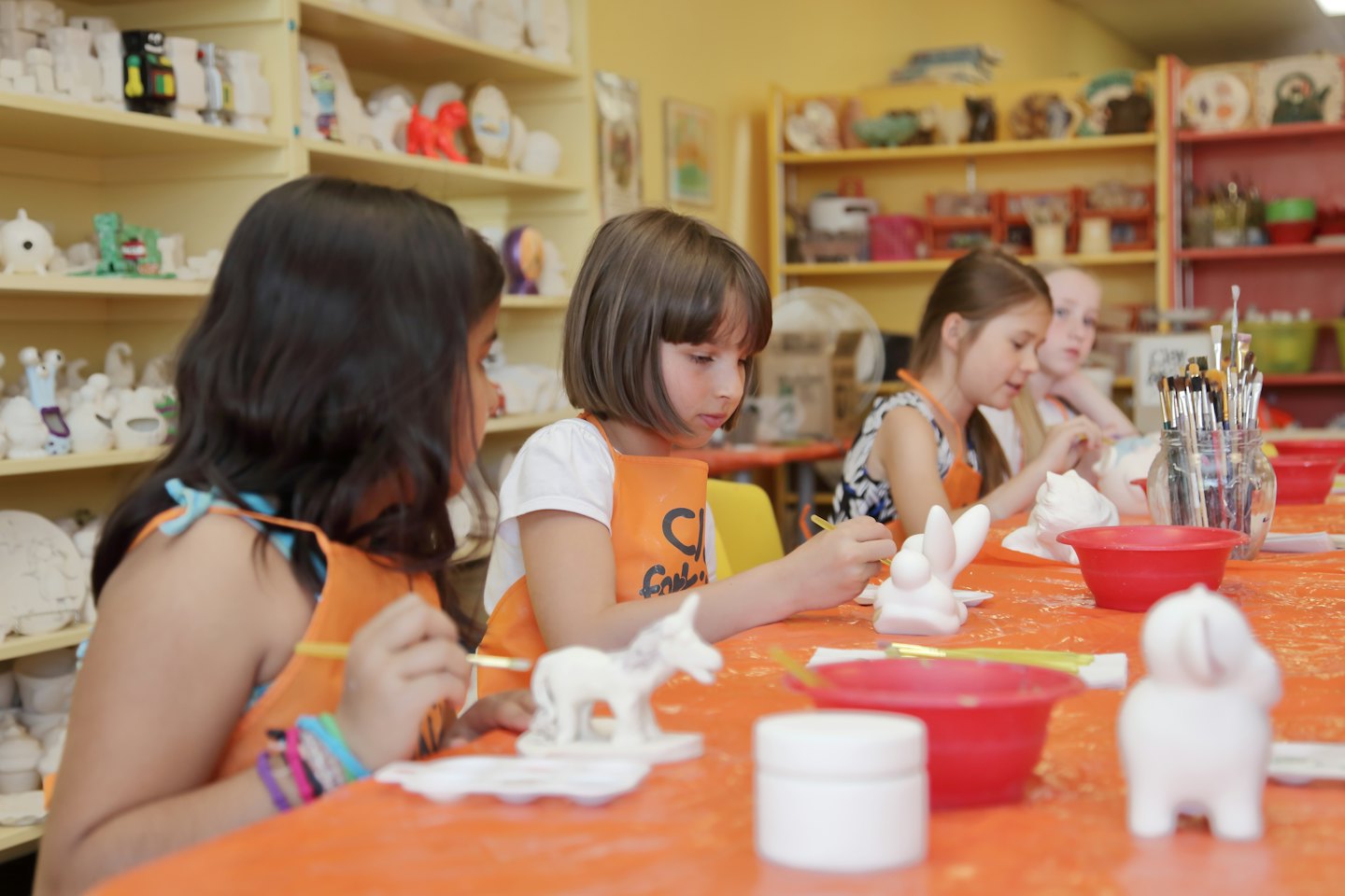 Bambini che dipingono statuette in ceramica in un luminoso studio d'arte.