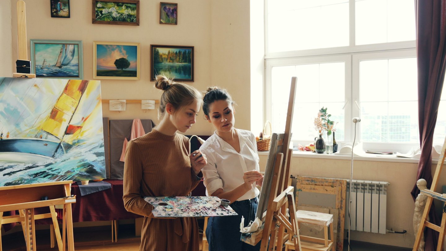 Un artista e uno studente dipingono una barca a vela in uno studio luminoso.