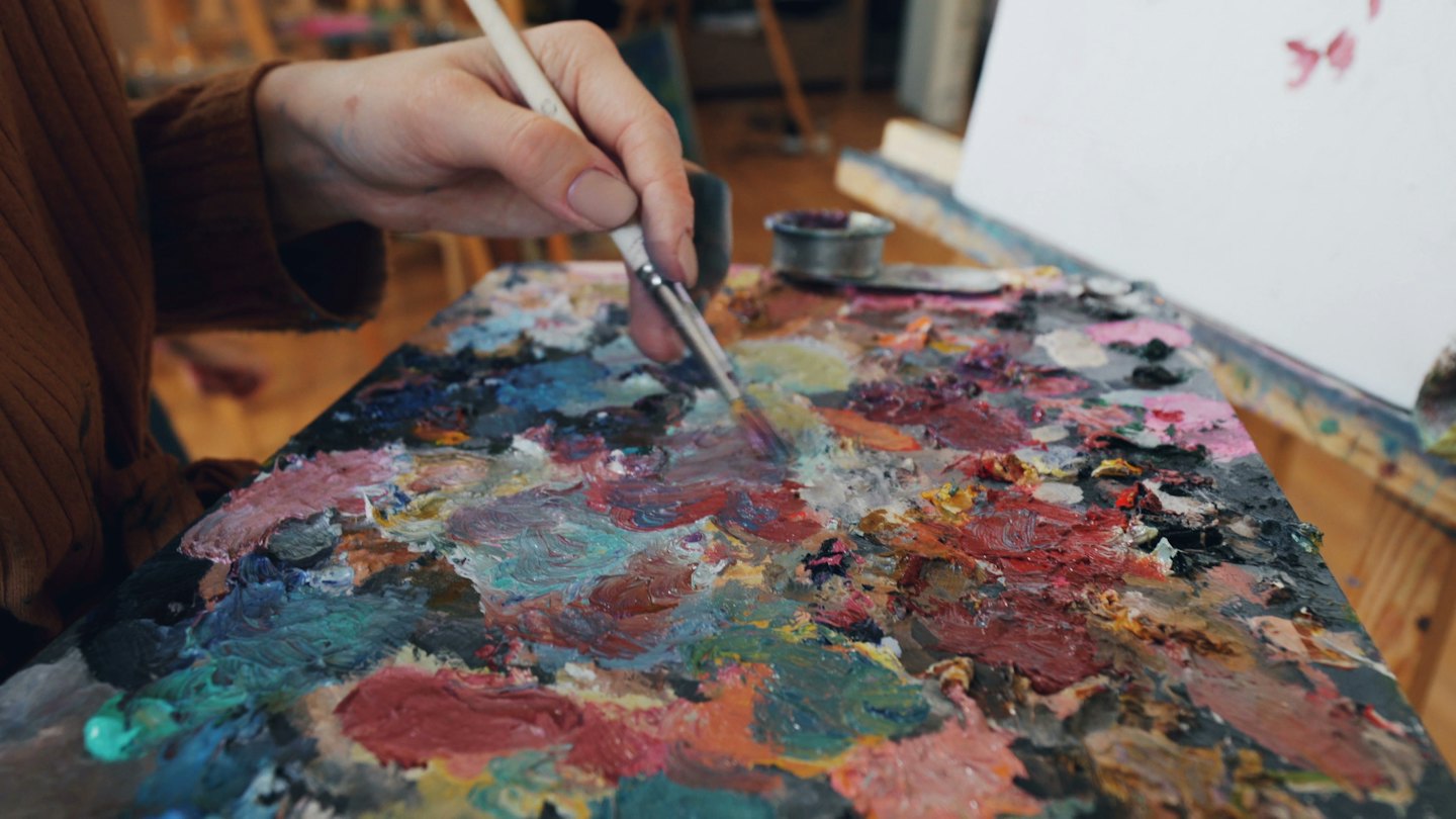 Mano di artista che mescola vernici colorate su una tavolozza di legno.
